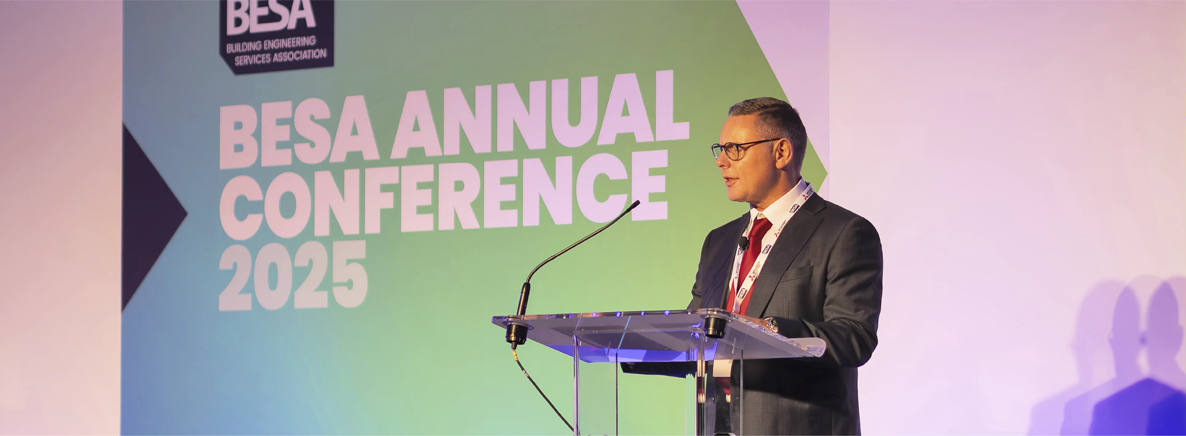 BESA Keynote speaker standing in front of BESA annual conference 2025 event designs.