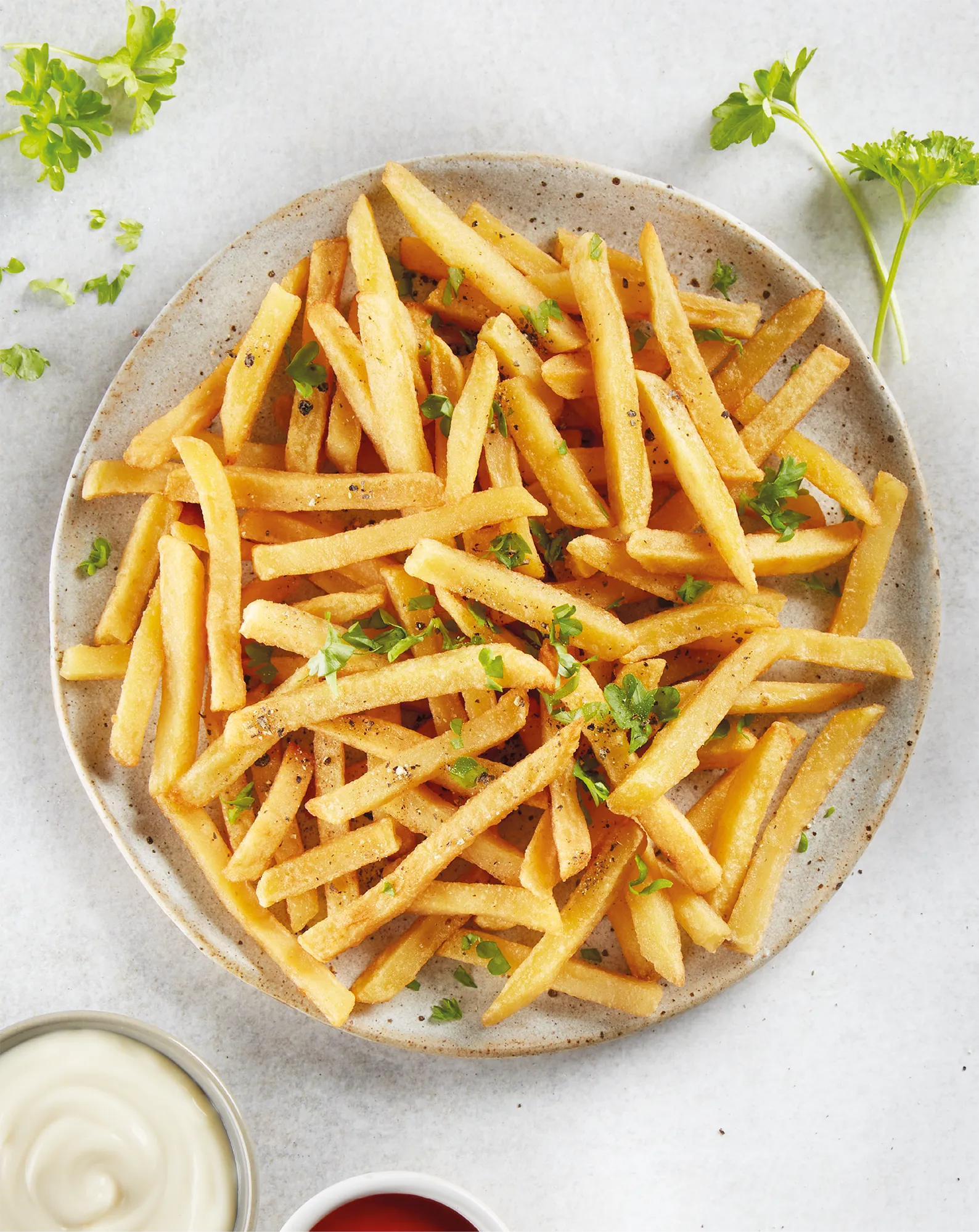 Overhead photography of French fries in a rustic bowl, surrounded by sprigs of parsley.
