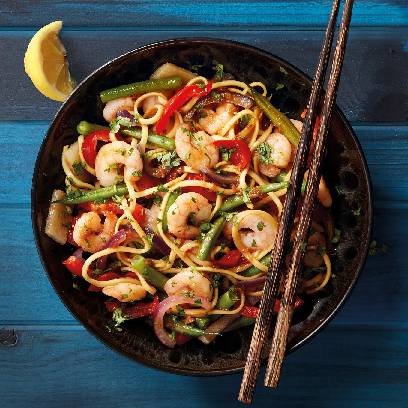 Styled food photography of a prawn and noodle stir fry. Shot in a black bowl, against a rustic, blue wooden background. 
Shot in-house by Stocks Taylor Benson.